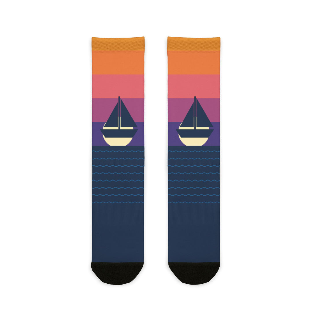 BlockBoundRI Sunset Sail nautical crew socks, orange-to-purple sunset fade with sailboat over navy striped foot, flat lay