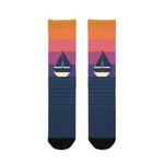 BlockBoundRI Sunset Sail nautical crew socks, orange-to-purple sunset fade with sailboat over navy striped foot, flat lay