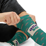 Close-up of hands pulling up a teal clam sock showing purple Quahog Squad on a cream band, Rhode Island socks