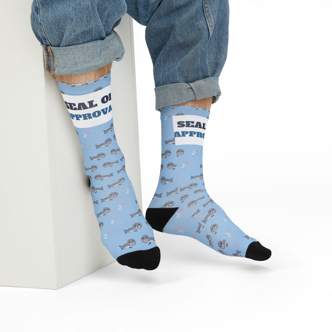 Model in rolled jeans seated on a white block wearing light blue Seal of Approval funny beach socks