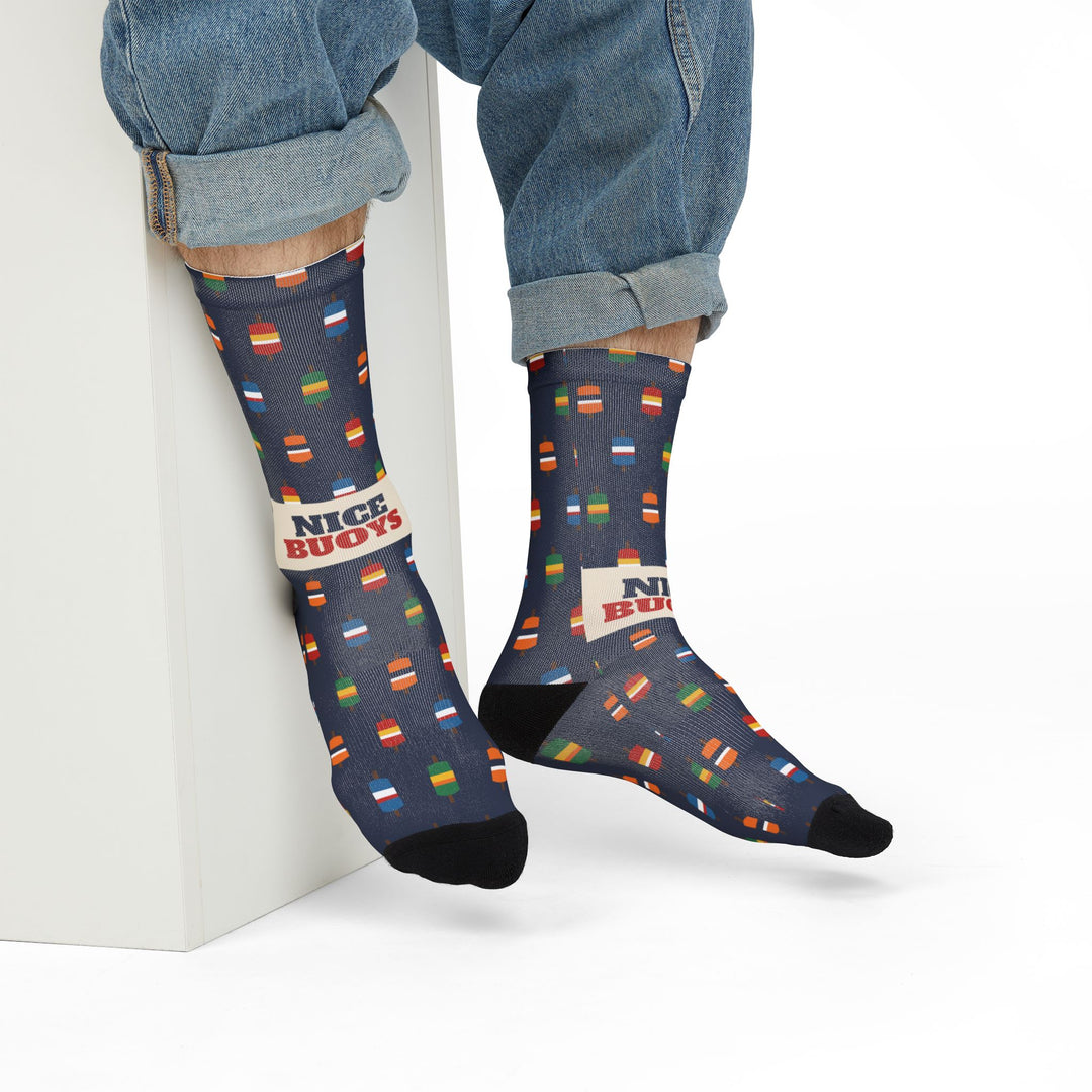 Model in rolled jeans sitting on a white block showing the Nice Buoys slogan on navy funny beach socks
