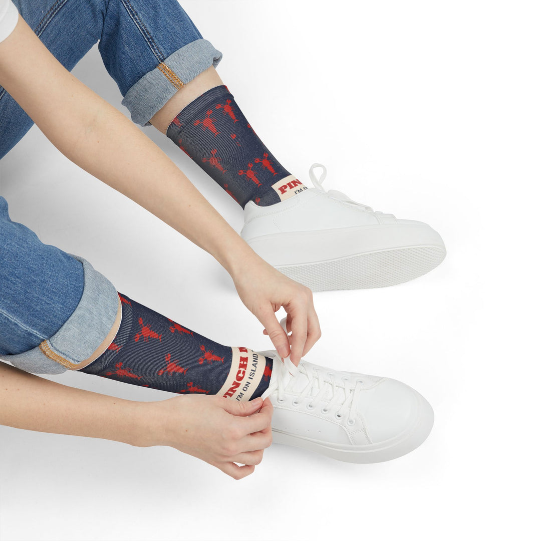 Seated model tying white sneakers while wearing navy Pinch Me lobster socks with cream band