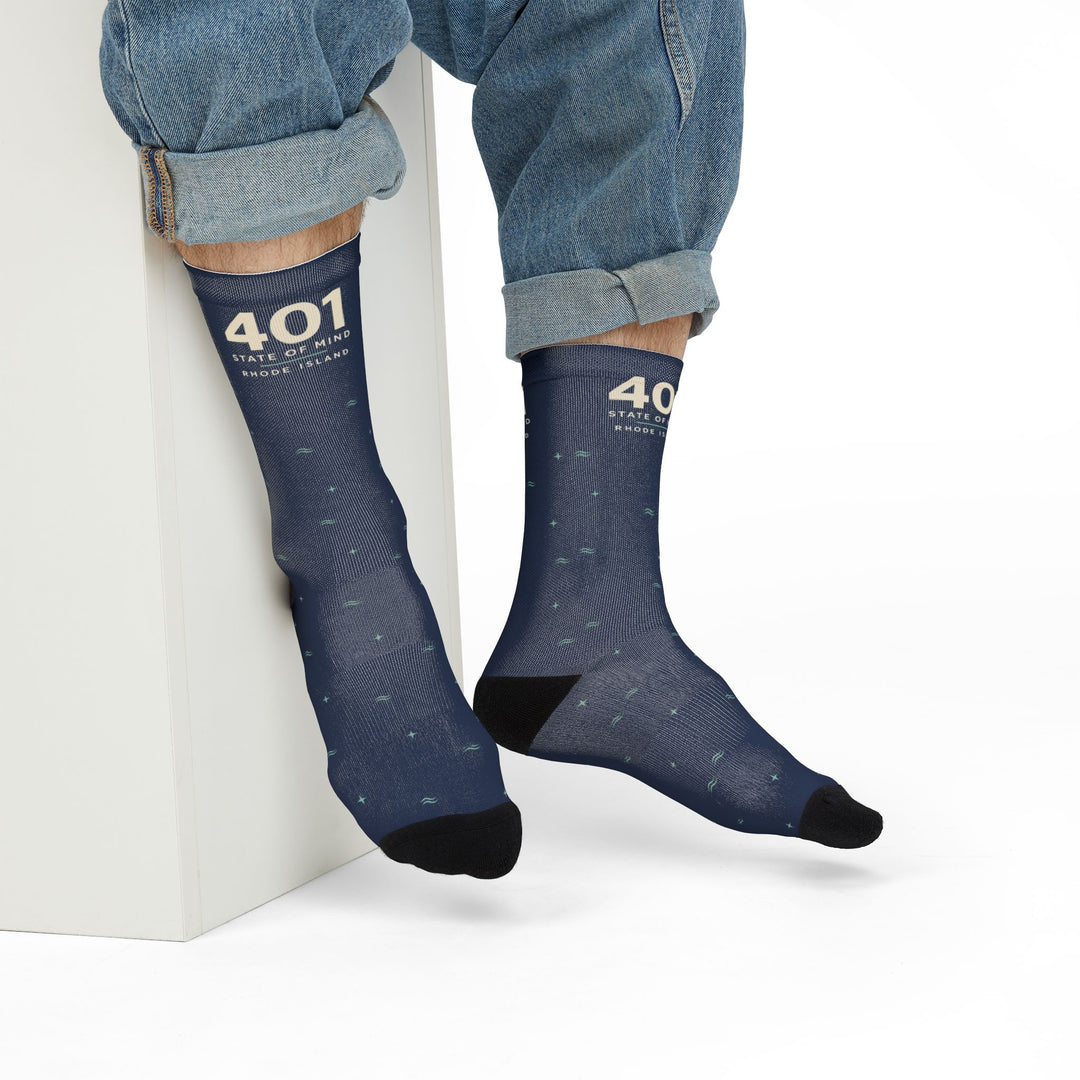 Model in rolled jeans seated on a white block wearing navy 401 State of Mind Rhode Island crew socks