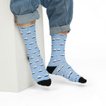 Seated model in rolled jeans showing light blue boat socks with rows of white sailboats