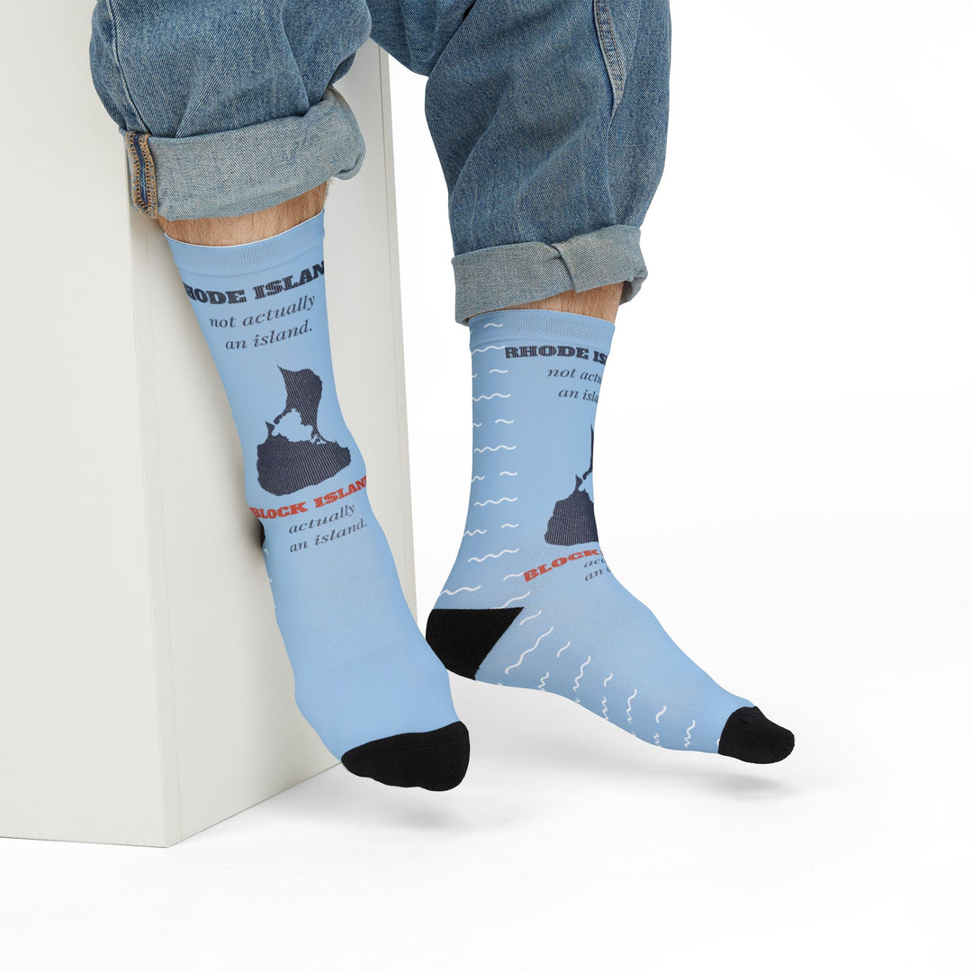 Model in rolled jeans seated on a white block wearing light blue Rhode Island socks with island map
