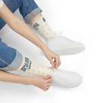 Seated model in rolled jeans and white sneakers pulling on white Small State. Big Attitude. Rhode Island socks